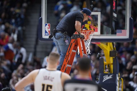 A worker uses a level to check the rim after it was bent by a dunk by Boston Celtics center Robert Williams III in the second half of an NBA basketball game against the Denver Nuggets, Sunday, Jan. 1, 2023, in Denver. (AP Photo/David Zalubowski)