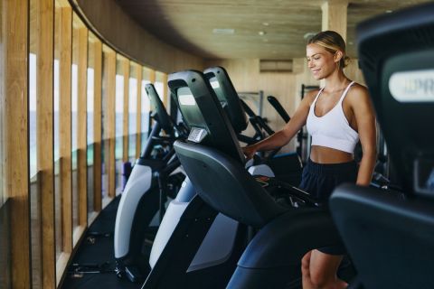 Happy athletic woman adjusting speed on treadmill during sports training in a gym.