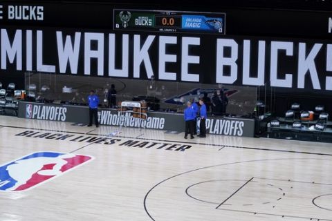 Officials stand beside an empty court before the scheduled start of an NBA basketball first round playoff game between the Milwaukee Bucks and the Orlando Magic, Wednesday, Aug. 26, 2020, in Lake Buena Vista, Fla. (AP Photo/Ashley Landis, Pool)