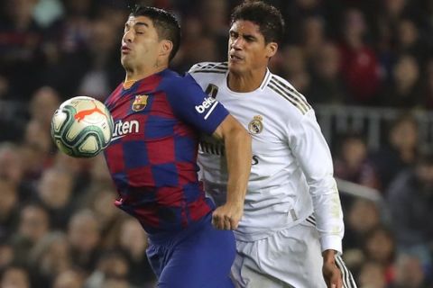 Barcelona's Luis Suarez, left, duels for the ball with Real Madrid's Raphael Varane during a Spanish La Liga soccer match between Barcelona and Real Madrid at Camp Nou stadium in Barcelona, Spain, Wednesday, Dec. 18, 2019. Thousands of Catalan separatists are planning to protest around and inside Barcelona's Camp Nou Stadium during Wednesday's "Clasico". (AP Photo/Emilio Morenatti)