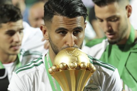 Algeria's Riyad Mahrez kisses the African Cup trophy end the African Cup of Nations final soccer match between Algeria and Senegal in Cairo International stadium in Cairo, Egypt, Friday, July 19, 2019. Algeria won 1-0. (AP Photo/Hassan Ammar)