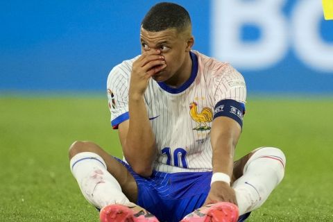 Kylian Mbappe of France sits on the pitch, hand over his bloody nose, as the referee holds the yellow card, during a Group D match between Austria and France at the Euro 2024 soccer tournament in Duesseldorf, Germany, Monday, June 17, 2024. (AP Photo/Andreea Alexandru)