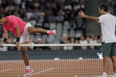 Rafael Nadal, left, jumps the net while Roger Federer watches on during their exhibition tennis match held at the Cape Town Stadium in Cape Town, South Africa, Friday Feb. 7, 2020. (AP Photo/Halden Krog)