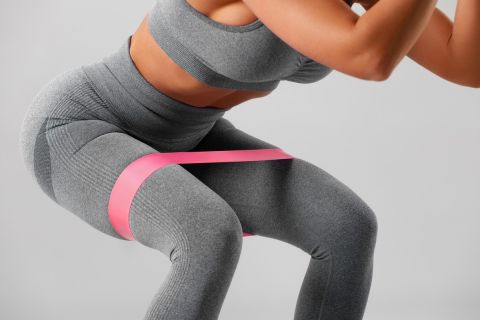 Athletic girl doing squats exercise for glute with resistance band. Fitness woman working out