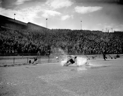 PA NEWS PHOTO 25/8/56 TOM FINNEY ENGLAND AND PRESTON NORTH END FORWARD IN A SHOWER OF WATER SPRAY WHICH ALMOST COMPLETELY HIDES CHELSEA LEFT-BACK BELLET AS THEY TUSSLE FOR THE BALL ON THE SOAKED PITCH AT STAMFORD BRIDGE, LONDON