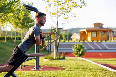 Young man performing lower back exercise on roman bench in an open air gym.