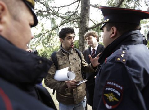 Activist David Khakim, center, talks to police officers after pulling out a banner protesting a recent prison sentence for a local environmentalist in front of the Olympic rings, Monday, Feb. 17, 2014, in central Sochi, Russia. Khakim was holding a one-man picket outside the city administration in central Sochi on Monday when two police officers took him away. Russia passed an ad-hoc law last year, banning public gatherings and rallies in Sochi during the Olympics. One-man pickets, however, are not covered by this law. Khakim was protesting the three-year prison sentence given last week to environmental activist Evgeny Vitishko for spray-painting a fence on a property in a forest where construction is banned. (AP Photo/David Goldman)