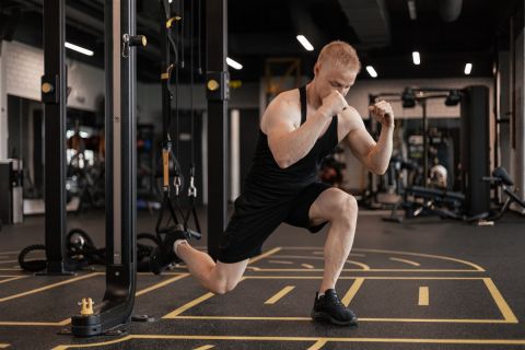 Strong sportsman doing bulgarian lunges in a gym with TRX