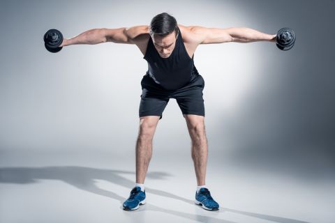 Attractive man athlete lifting dumbbells on grey background