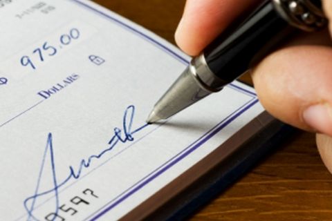 Close up of a hand signing a check.  Please note that the signature is fictitious.