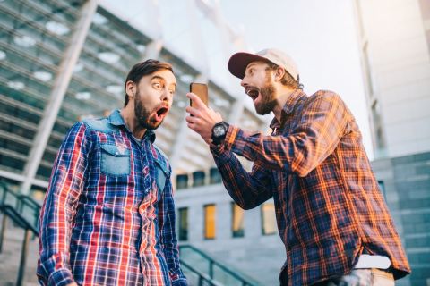 Two friends showing sincere emotions of joy about victory in online lottery. Men being happy winning a bet in online sport gambling application with football stadium on the background.