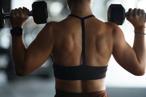 Back side, strong muscular young woman lifting dumbbell weights at the gym, doing exercises with dumbbell, fitness muscular body