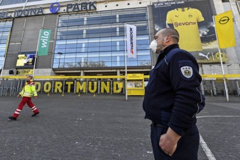 Security with face masks stand in front of the Signal Iduna Park, Germany's biggest stadium of Bundesliga soccer club Borussia Dortmund, where a temporary coronavirus treatment center opened today in Dortmund, Germany, Saturday, April 4, 2020. Instead of the originally scheduled today football clash between Dortmund and Bayern, parts of the stadium were turned into a medical center for outpatient treatment and consultation. The new coronavirus causes mild or moderate symptoms for most people, but for some, especially older adults and people with existing health problems, it can cause more severe illness or death. (AP Photo/Martin Meissner)