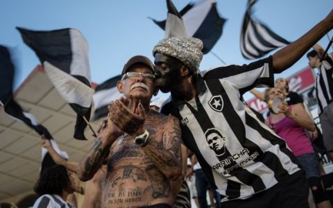 TO GO WITH AFP STORY by Javier Tovar
Brazilian football club Botafogo fan Delneri Martins Viana (L), a 69-year-old retired soldier, is kisses by another fan of the team during a match at Sao Genario stadium in Rio de Janeiro, Brazil, on January 21, 2014. Delneri has 83 tattoos on his body dedicated to Botafogo and describes himself as the club's biggest fan.   AFP PHOTO / YASUYOSHI CHIBA