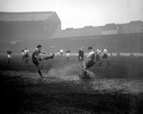 In a cloud of spray Chelsea's Peter Brabrook (r) takes a kick on the water logged pitch, past Bolton Wanderers' Ralph Gubbins (r).