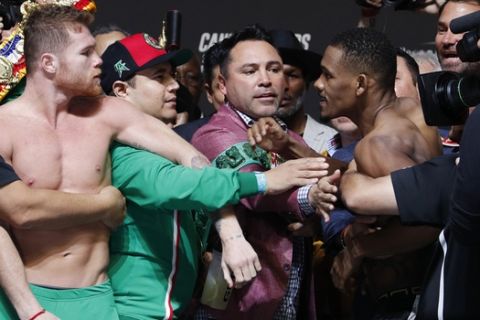 Oscar De La Hoya, center, gets between Canelo Alvarez, left, and Daniel Jacobs during a weigh-in for the middleweight title boxing match between Alvarez and Jacobs, Friday, May 3, 2019, in Las Vegas. The two are scheduled to fight Saturday in Las Vegas. (AP Photo/John Locher)