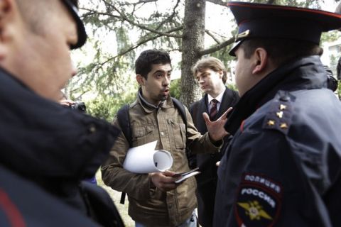 Activist David Khakim, center, talks to police officers after pulling out a banner protesting a recent prison sentence for a local environmentalist in front of the Olympic rings, Monday, Feb. 17, 2014, in central Sochi, Russia. Khakim was holding a one-man picket outside the city administration in central Sochi on Monday when two police officers took him away. Russia passed an ad-hoc law last year, banning public gatherings and rallies in Sochi during the Olympics. One-man pickets, however, are not covered by this law. Khakim was protesting the three-year prison sentence given last week to environmental activist Evgeny Vitishko for spray-painting a fence on a property in a forest where construction is banned. (AP Photo/David Goldman)