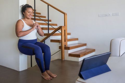 Portrait shot of an attractive Malaysian woman doing wall sit exercise in her living room during Covid 19 pandemic