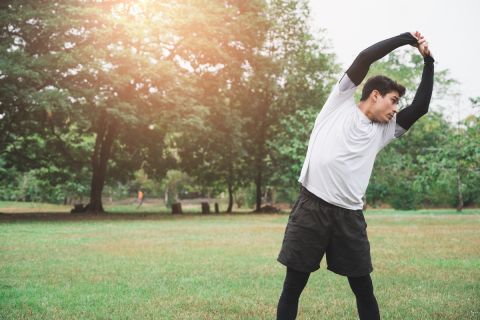 Young man runner stretching for warming up before running or working out in park.