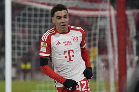 Bayern's Jamal Musiala celebrates after scoring the opening goal during the German Bundesliga soccer match between FC Bayern Munich and TSG 1899 Hoffenheim at the Allianz Arena in Munich, Germany, Friday, Jan. 12, 2024. The words in the center of the Bayern shirts translate to "Thanks Franz' which is in honour of Franz Beckenbauer, a club legend for Bayern as a player, coach and president, whose death at the age of 78 prompted tributes from across the soccer world but has left a particularly deep impression on Bayern the team where he spent so much of his decades-long career. (AP Photo/Matthias Schrader)