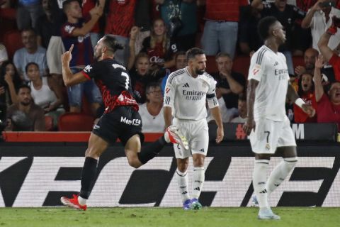 Mallorca's Vedat Muriqi, left, runs past Real Madrid's Dani Carvajal, left and Vinicius Junior while celebrating after scoring his side's first goal during a Spanish La Liga soccer match between Mallorca and Real Madrid at the Son Moix Stadium in Palma de Mallorca, Spain, Sunday, Aug. 18, 2024. (AP Photo/Francisco Ubilla)