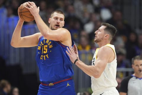 Denver Nuggets center Nikola Jokic, left, looks to pass the ball as Utah Jazz forward Drew Eubanks defends in the second half of an NBA basketball game Saturday, Nov. 2, 2024, in Denver. (AP Photo/David Zalubowski)