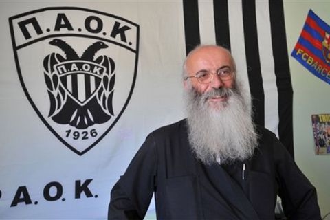 In this Wednesday, June 8 , 2009 photo, Orthodox priest Father Christos Mitsios poses in  front of a banner of Greek football club PAOK Thessaloniki, in Thessaloniki, Greece. Many hard-core football fans follow the sport religiously, and Father Christos Mitsios is no exception. The 51-year-old Greek Orthodox priest has become a mainstay in the hardcore section at PAOK Thessaloniki matches, cheering on the team and offering help and guidance to many of Greece's most fervent supporters in the fearsome Gate 4 section of the Toumba Stadium. Church elders stripped Father Christos of his administrative responsibilities, angry at his blunt refusal to stop attending matches. But a campaign with 18,000 followers launched on the social media site Facebook last year helped insure that his punishment stopped there. (AP Photo/Nikolas Giakoumidis)